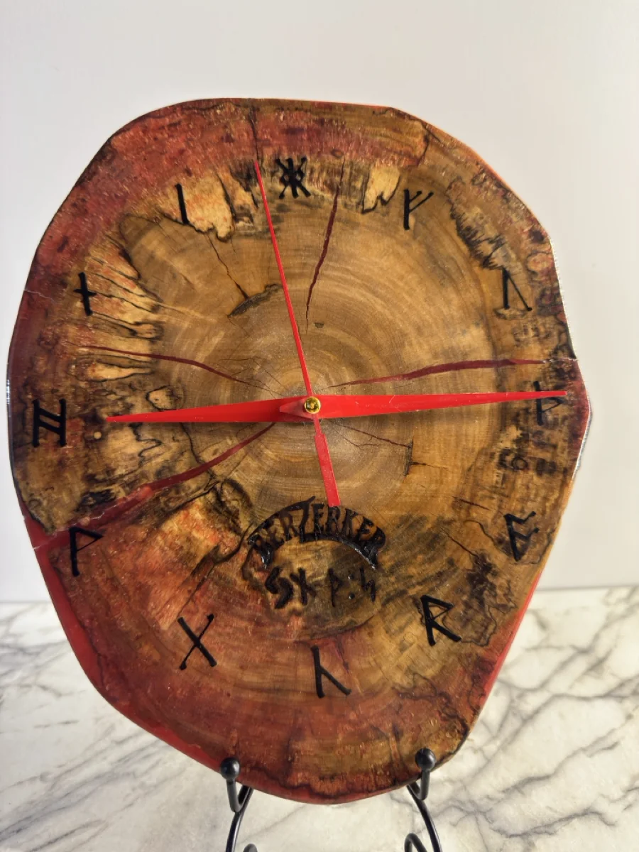 Front view of the wood clock showing red hands, dark symbols, end-grain rings, and its irregular outer form.
