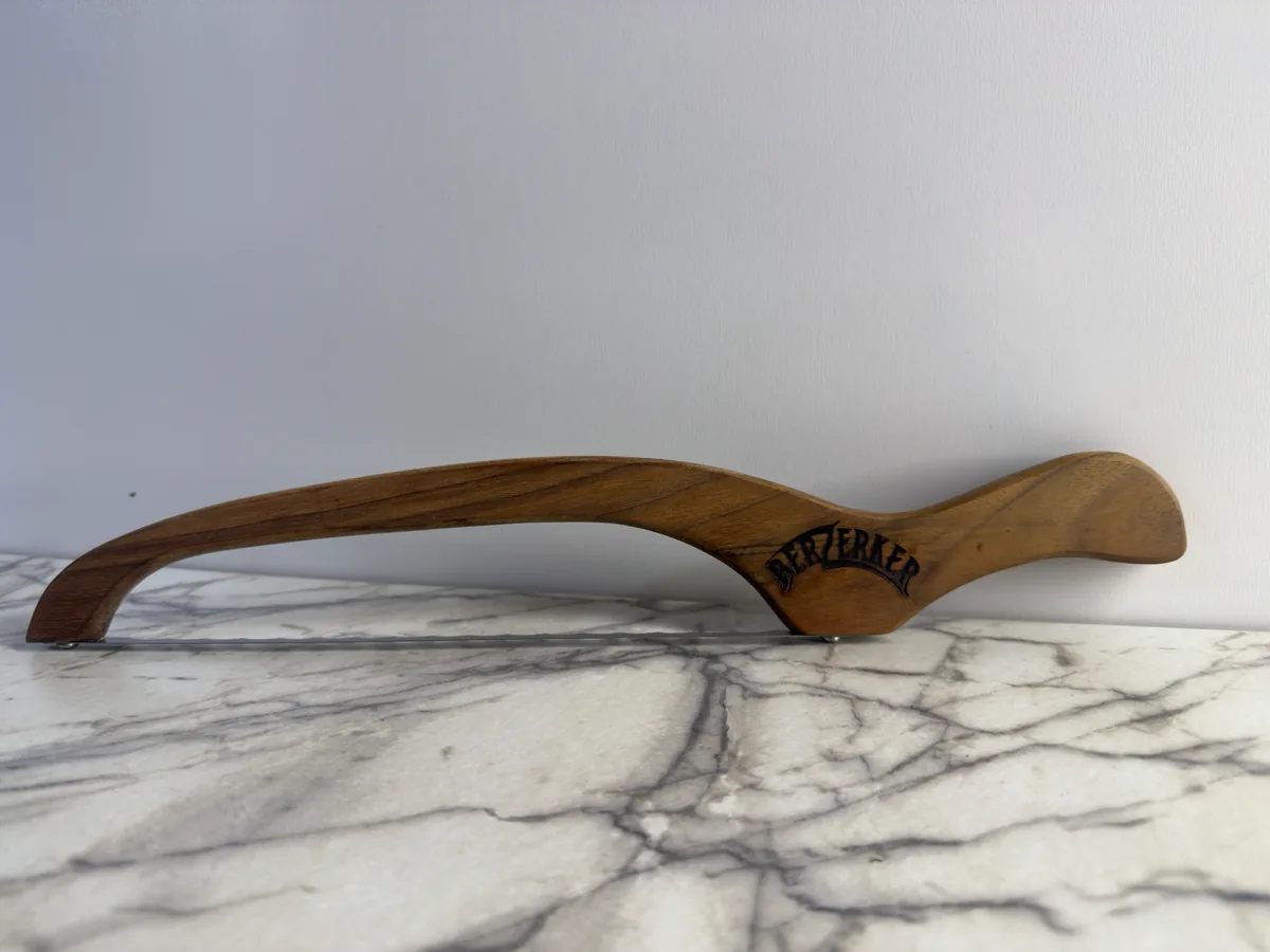 Long curved wood knife sheath with a dark maker's mark on a light surface.